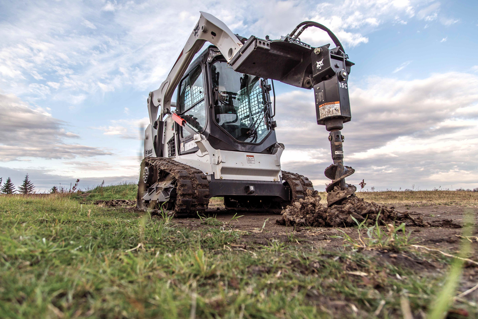 Bobcat mit Erdbohrer beim Bohren von Fundamentlöchern für ein Gewächshaus